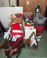 Two brown reindeer statues (one large with broken antler, one smaller intact) in front of red storage tubs with various boxed decorations