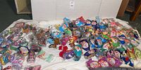 Wide view showing over 100 McDonalds Happy Meal prize toys including many Ty Beanie Babies and other franchise figures in original plastic bags.