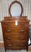 Front view of solid walnut highboy dresser with attached oval mirror, showing carved drawer pulls and overall appearance.