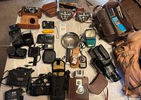Full collection laid out on floor including cameras, flashes, light meters, video cameras, and accessories.