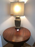 Full view of the solid wood round table with the Asian brass lamp on top, showing surface wear on table.