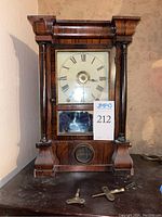 Front view of the Seth Thomas wooden mantle clock showing clock face with Roman numerals and porthole window at bottom, includes two metal winding keys placed in front.
