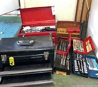 Wide view showing multiple toolboxes and socket sets including black Craftsman metal toolbox, red metal toolbox, and small yellow plastic toolbox with mixed sockets.