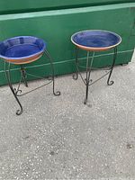Two blue glazed terra cotta plant stands on wrought iron tripod bases, showing front and side views.