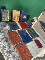 Full view of all twelve antique books laid out on a lace tablecloth, showing colorful covers and various sizes.