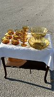 Photo showing all 12 amber glass pieces on a white tablecloth, including the 6 side bowls, 4 fruit nappies, and the 2 large serving bowls.