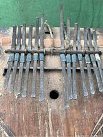 Close-up of the metal tines of the kalimba attached to the wooden sound box. The tines are dark metal, some bound with blue strings.