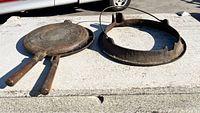 Cast iron grittle pan with wooden handles upright beside socket base on concrete surface.