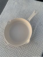 Top view of cream/beige enamel cast iron frying pan on textured cloth showcasing the circular cooking surface and handle shape.