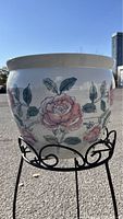 Close-up of the decorated ceramic flower pot showing hand-painted pink roses and leaves.