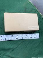 Beige protective plastic case for digital micrometer with GE Genuine logo shown alongside a ruler for size reference.