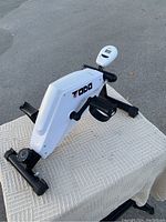 Side view of the compact white and black magnetic exercise bike labeled 'Todo' with pedals and adjustable resistance knob.