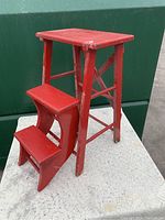 Front angle of the red hardwood fold-out step stool showing two steps and flat top.