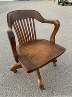 Front view of oak swivel office chair showing seat, armrests, backrest slats, and leg base with casters.