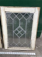 Photo showing one window with diamond-shaped leaded glass design and wooden white frame
