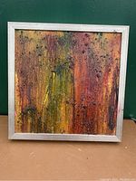 Front view of the mixed media abstract painting showing textured orange, yellow, and black colors with a silver frame.