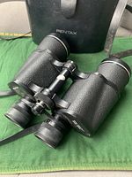 Close-up photo of the Pentax binoculars showing textured black body and center focus knob.