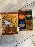 Two small decorative autumn/fall flags placed flat on the floor showing all designs clearly.