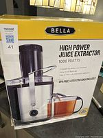 Box front showing brand Bella and high power juice extractor with 1000 watt motor, 2 speeds, wide 5 inch feed tube, BPA-free 1-liter container included.