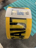 Roll of yellow caution tape showing the black lettering, new condition, label with lot number affixed.