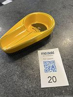 Yellow ceramic cigar ashtray on black countertop, showing top angled view with the ash bowl and cigar rests, alongside a lot number card.