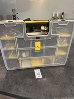 Full front view of the translucent plastic hardware organizer case with yellow dividers and black handle, closed with a yellow latch.