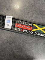 Close-up image showing Appleton Jamaica Rum branded bar mat with textured surface and vibrant logo including Jamaican flag colors.