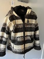 Front view of the large wool knit coat with black, white, and gray stripes, hood with braided drawstrings, front pockets, and zipper closure.