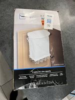Box of Mainstays in-cabinet garbage bin holder with 5 gallon capacity, white metal frame and liner bag shown from two angles