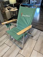 Front view of green Tommy Bahama patio chair showing wooden armrests, blue foam handle grip, and embroidered logo