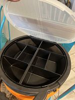 Close-up of interior black hardware organizer tray with multiple compartments inside orange pail.