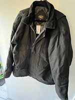 Photo showing full black men's winter coat hanging, displaying front and part of the side to reveal structure and style.