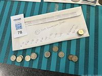 25 Canadian dimes partially laid out on a teal surface next to a white envelope listing years: 1943, 1945, 1948, 1951, 1952, 1955, 1960, 1965, 1966.