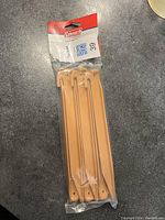 Set of 8 light brown polyethylene tent pegs in original sealed plastic packaging with Coleman label.