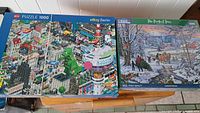Two puzzle boxes side by side on wooden surface: Pixorama city scene on left, The Perfect Tree winter scene on right