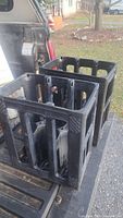 Two black plastic reusable containers placed on vehicle tailgate outdoors, each container with six slots for wine bottles.