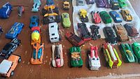 Photo showing multiple colorful die-cast Hot Wheels cars arranged on a wooden table surface.