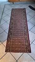 Photo of the full length of a 6.5 foot antique style floor runner rug on tiled floor showing pattern and colors.