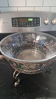 Clear glass bowl with cut pattern on metal stand with holly berry decoration, shown on a stove top.