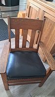 Front view of the antique solid wood armchair showing wood slat backrest and black cushion seat with nailhead trim.