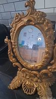 Front view of vintage ornate cast iron gold mirror showing intricate floral and scrollwork design around oval mirror.