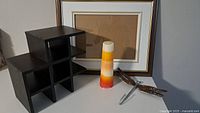 Wooden picture frame with matte, small black wooden shelf, new gradient candle, and metal dragonfly wall hook arranged together
