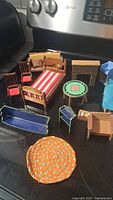 Image showing a variety of miniature doll house furniture including a striped bed, chairs with cushions, a small table, couch pieces, and an orange rug.
