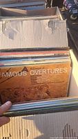 Top view of cardboard box filled with vinyl records, showing 'Famous: A Concert of Overtures' album cover.