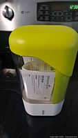 Front angle of Pampered Chef Herb Keeper showing yellow lid, clear water reservoir, and white base with instruction paper inside