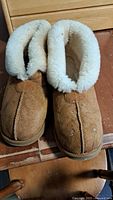 Pair of brown suede slippers with white fleece lining and cuff, showing spots on the front.