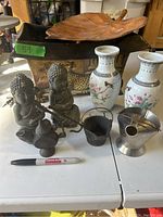 Photo showing Buddha statues, porcelain vases, cast iron pot and teapot, metal container, and leaf display on table.