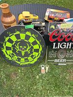 Photo showing wooden vase, yellow car bank, dart board, Coors Light sign, and two bottle openers on green grass