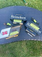 Three vintage bar signs including two Heineken and one Miller High Life arranged on a black woven surface outdoors. Two Heineken signs stacked, one Miller High Life sign with digital clock display, cords visible and taped.