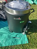 Char-Broil black oil-less turkey fryer with handles, control valve and attached hose, resting on green tarp outdoors.